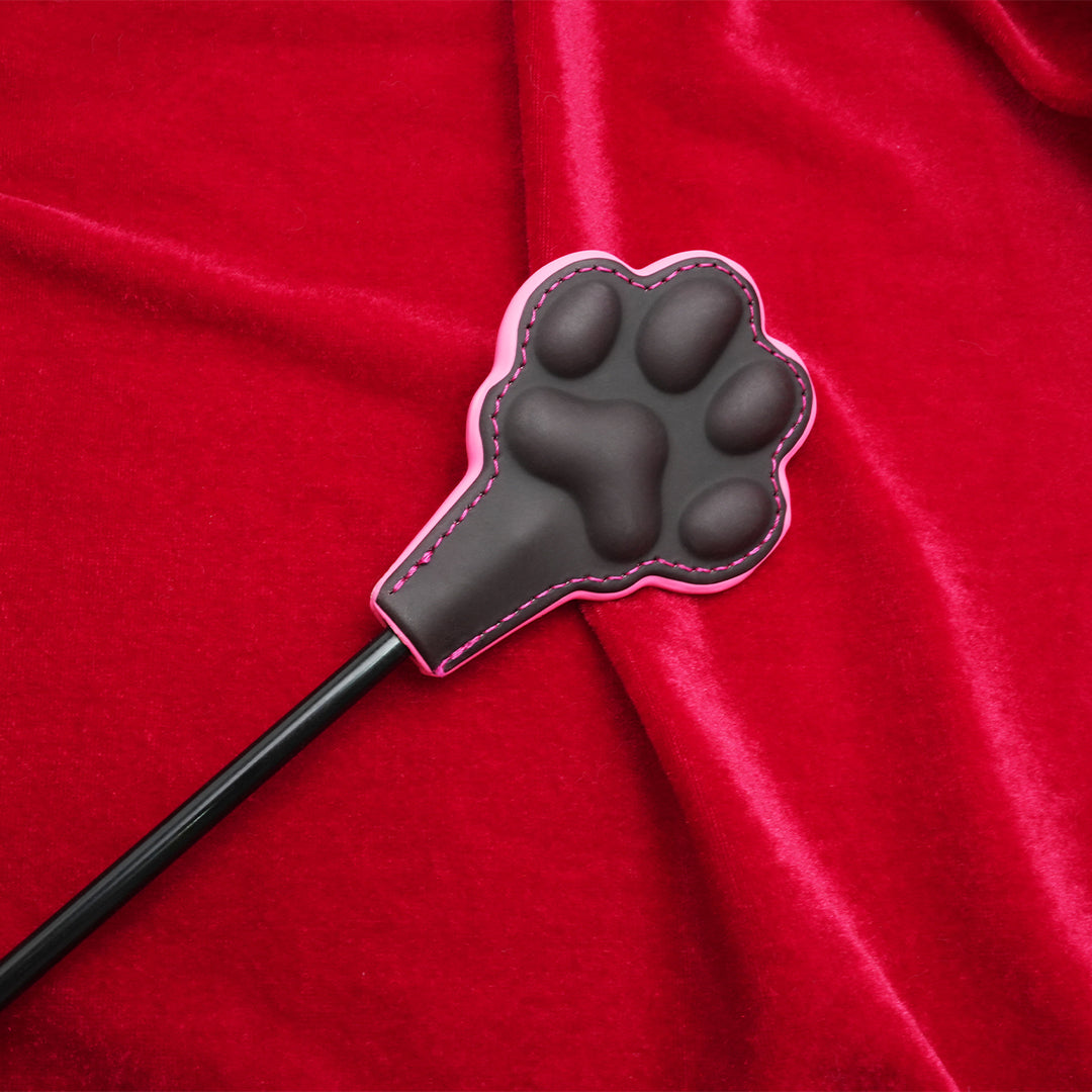 Black cat paw whip paddle with pink stitching on red velvet.