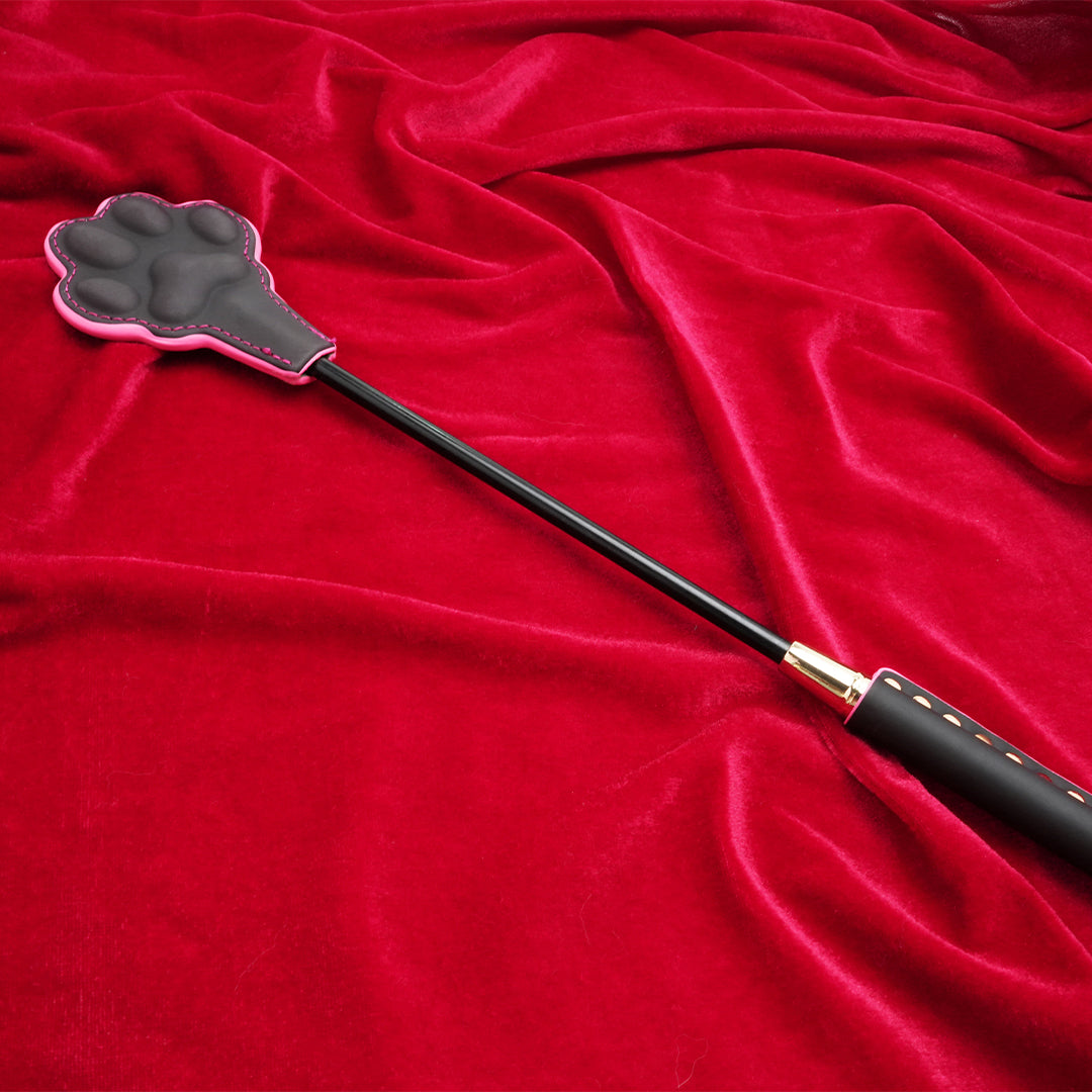 Black Cat Paw Whip Paddle with pink trim on red velvet.