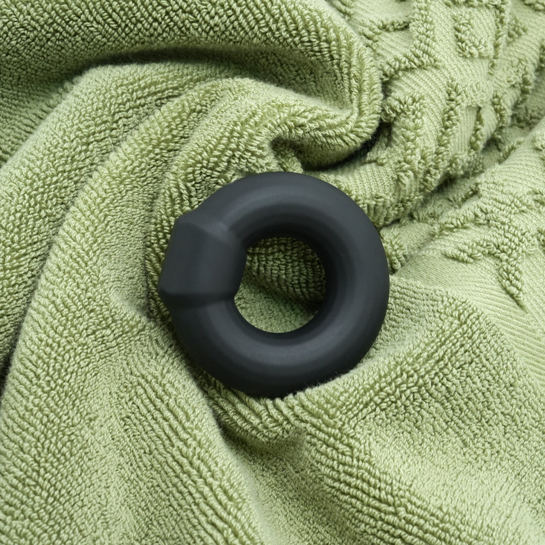 Donut silicone cock ring in black, on textured green towel.