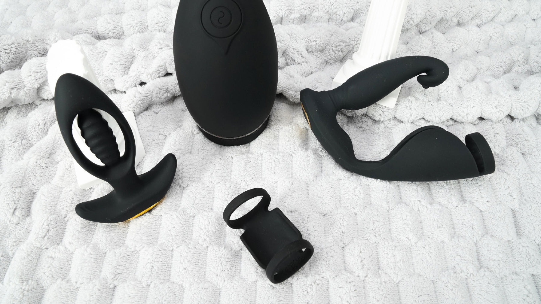 Four black prostate vibrator sex toys are placed on a grey blanket