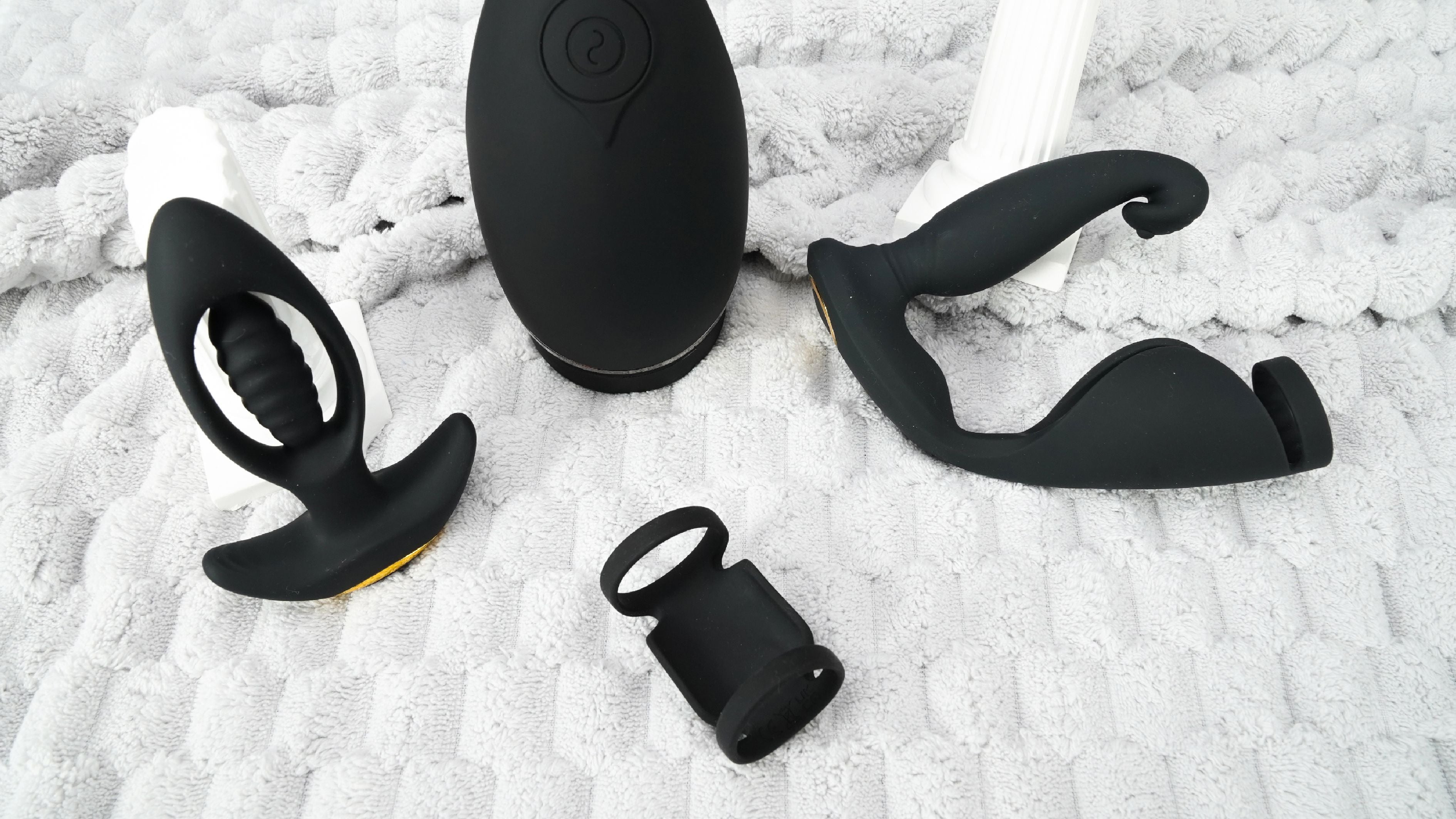 Four black prostate vibrator sex toys are placed on a grey blanket