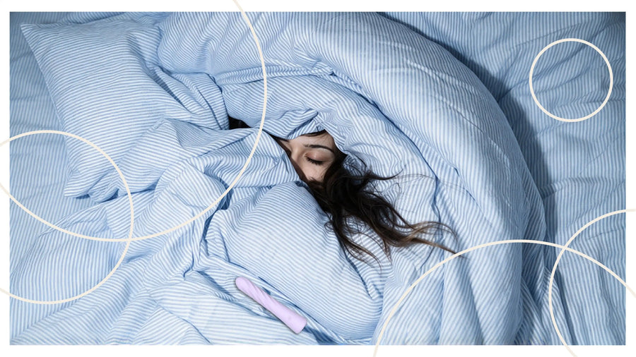 Woman resting under blue bedding beside a lavender vibrator